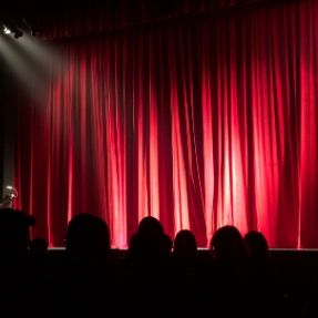 Theatre audience looking at a closed red curtain